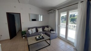 A modern living room with a grey sofa, a coffee table, and a large sliding glass door leading to a balcony.