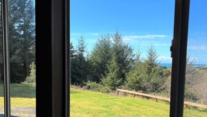 A view through a window of a grassy outdoor area with trees and a wooden fence. - Betty's Beach House Bungalow (Brookings)