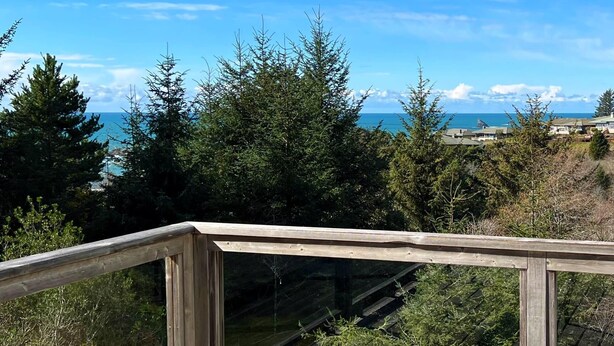 A wooden deck overlooking a coastal area with dense greenery and a clear view of the ocean. - Betty's Beach House Bungalow (Brookings)