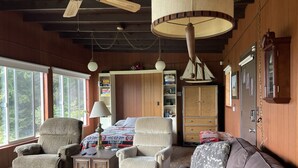 A cozy living room with a large window, a ceiling fan, a bookshelf, and a bed with a patterned bedspread. - Betty's Beach House Bungalow (Brookings)