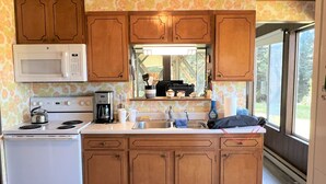 A compact kitchen with wooden cabinets, a microwave, a stove, and a sink. - Betty's Beach House Bungalow (Brookings)
