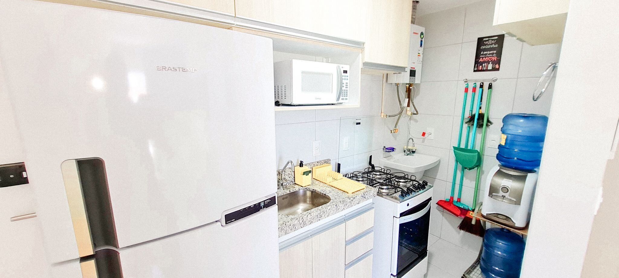 Una cocina con un refrigerador blanco, un microondas, un lavamanos, una estufa y un dispensador de agua.