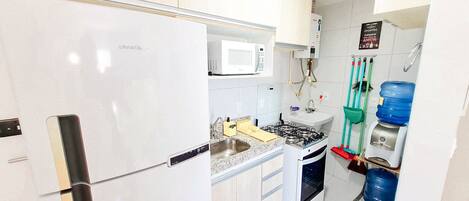Una cocina con un refrigerador blanco, un microondas, un lavamanos, una estufa y un dispensador de agua.