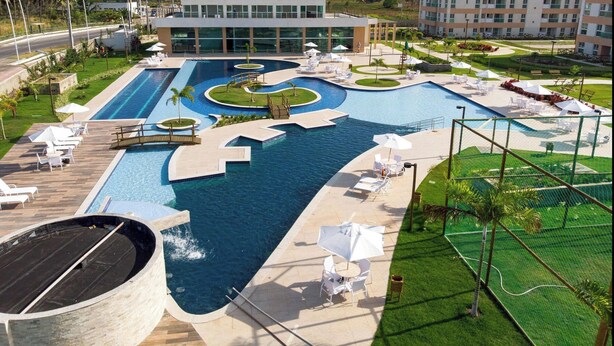 A large outdoor swimming pool with multiple lanes, surrounded by lounge chairs and umbrellas. - Flats no Muro Alto Clube (Ipojuca)