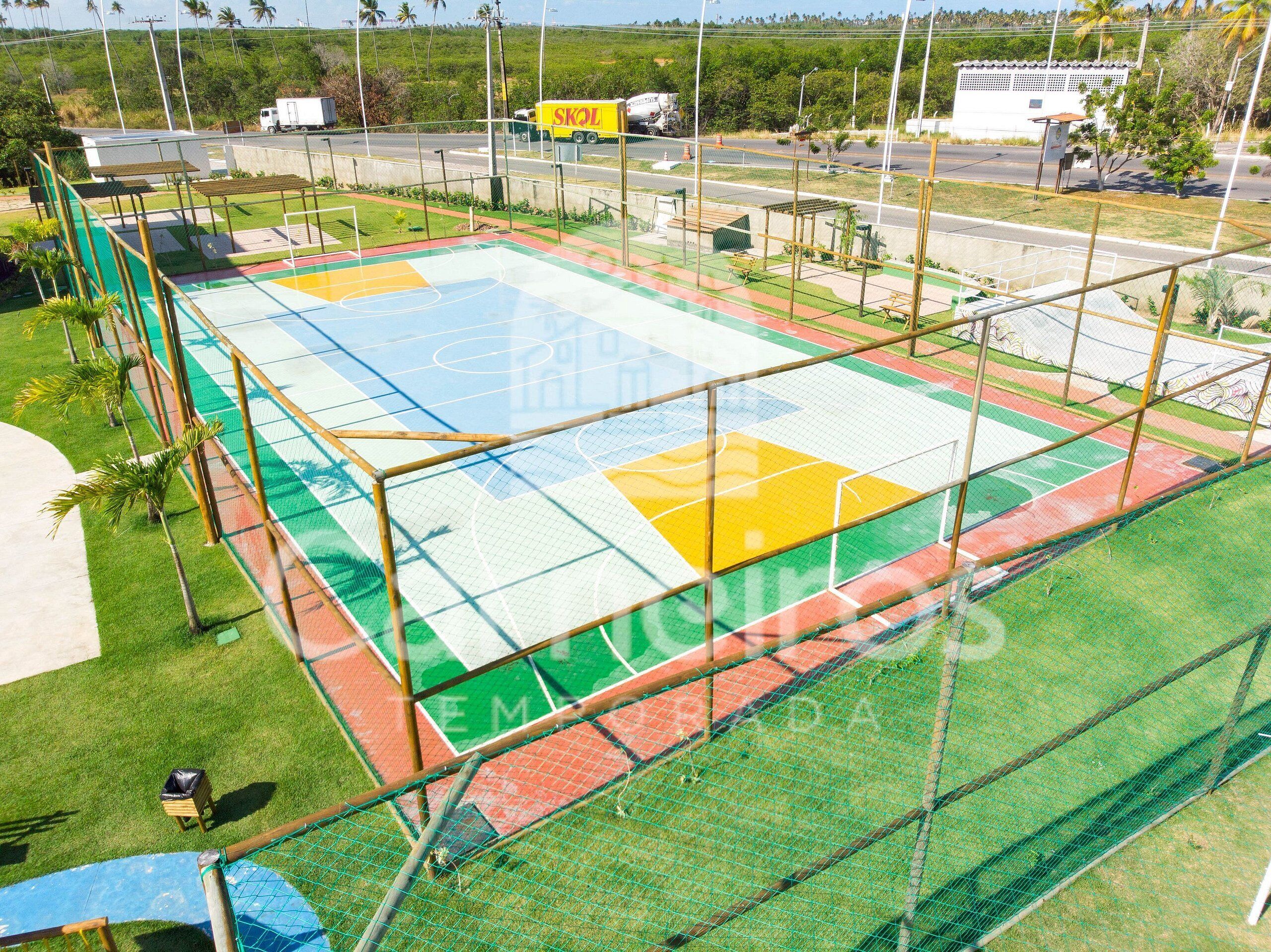 A sports court with a netted enclosure, surrounded by a grassy area and a road with vehicles.