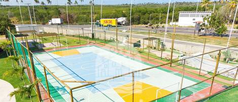 A sports court with a netted enclosure, surrounded by a grassy area and a road with vehicles.