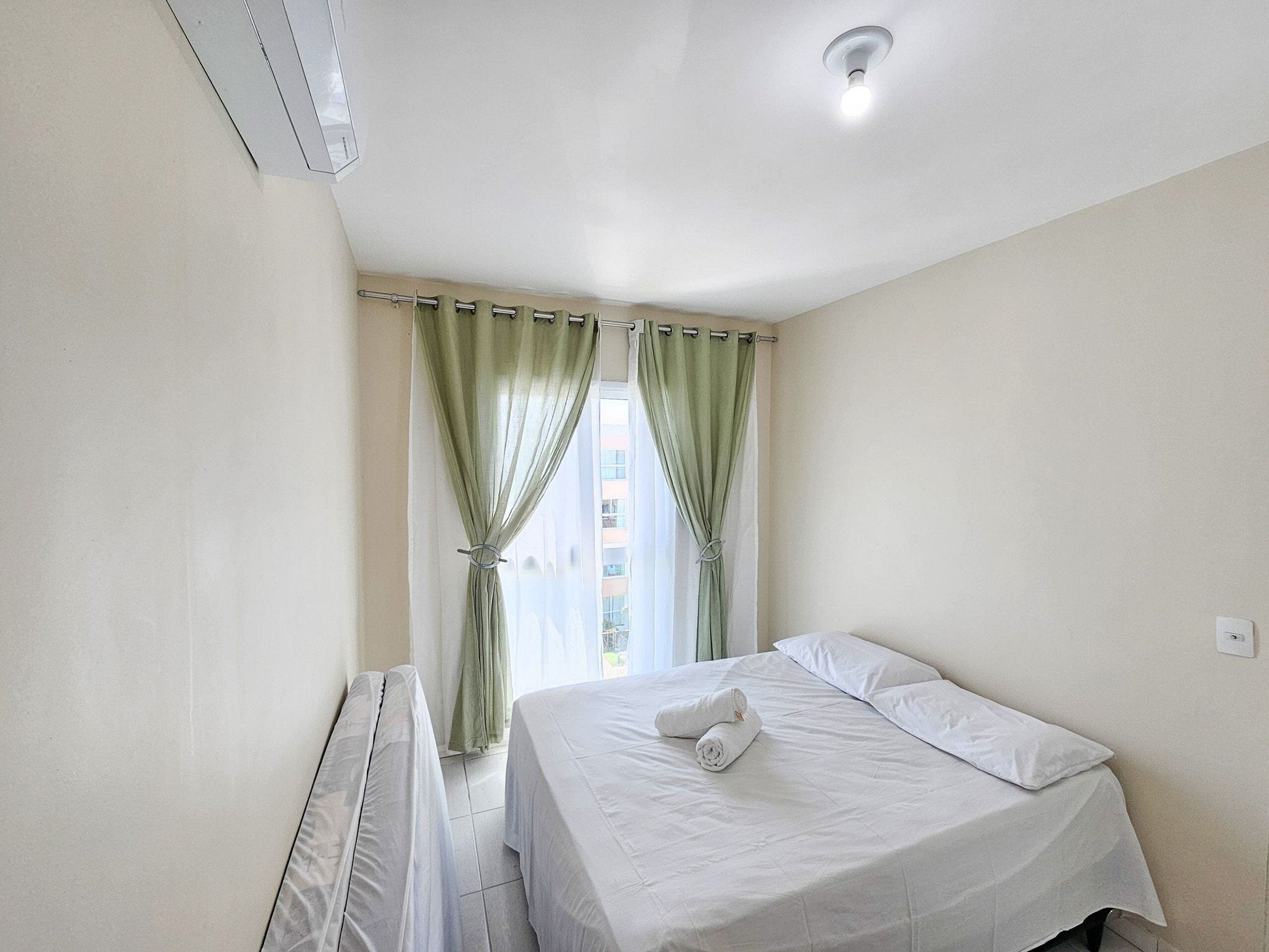 A clean, well-lit hotel room with a bed, a radiator, and a window with green curtains.