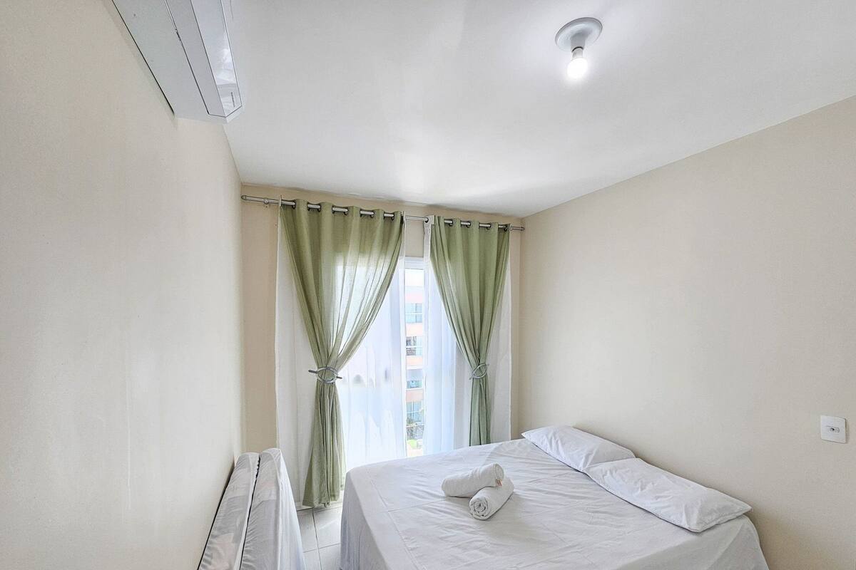 A clean, well-lit hotel room with a bed, a radiator, and a window with green curtains.