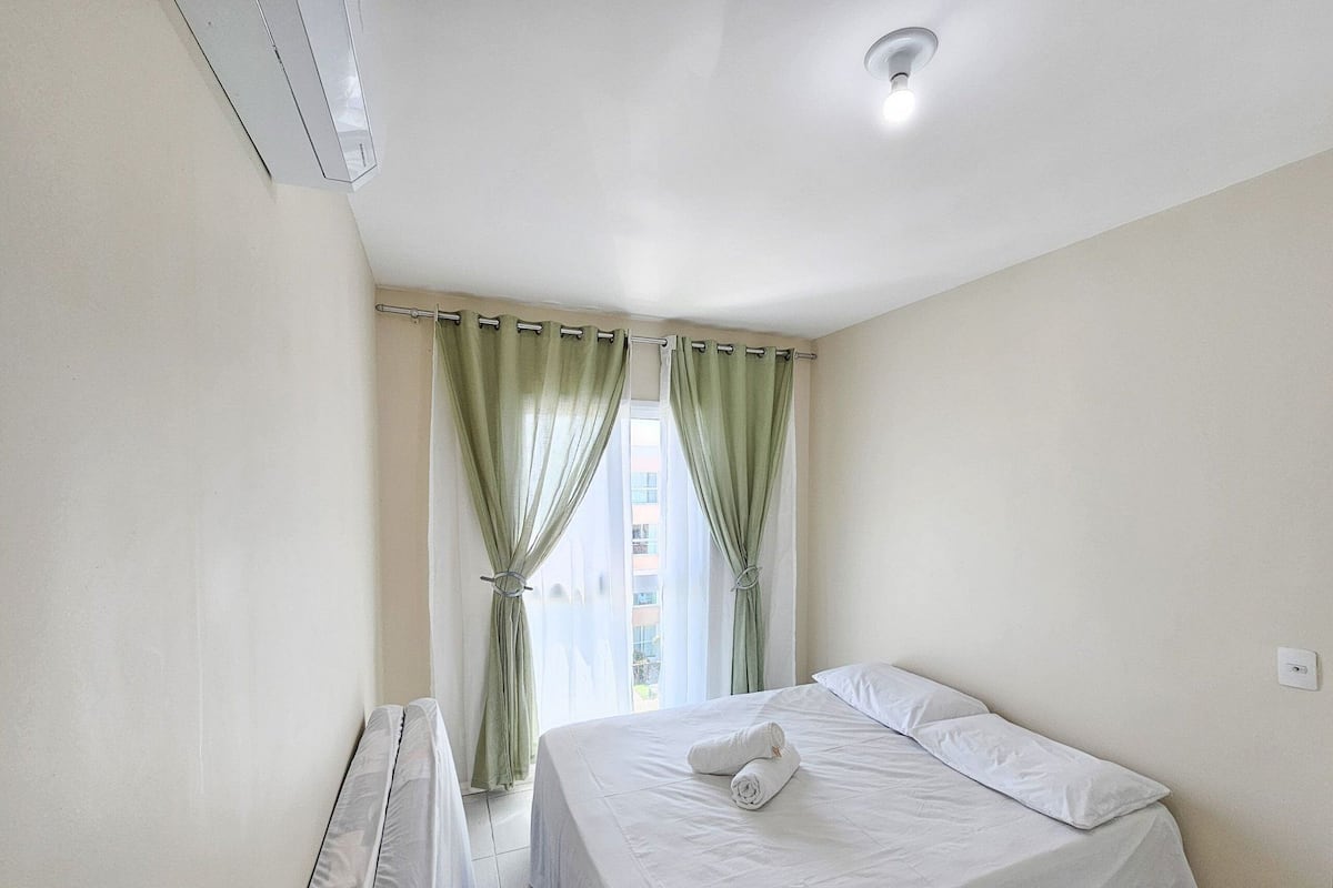 A clean, well-lit hotel room with a bed, a radiator, and a window with green curtains.