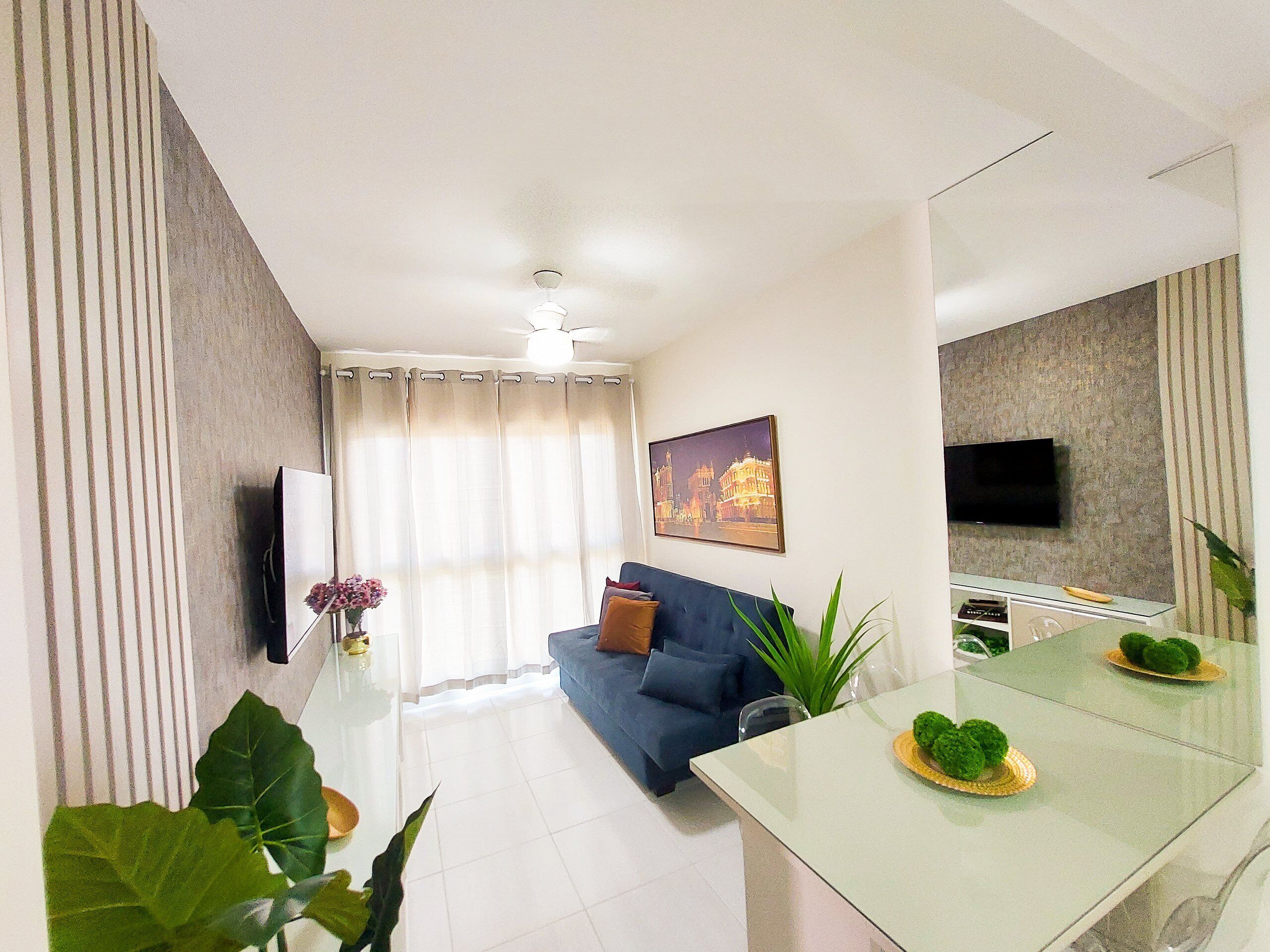 A modern living room with a sofa, a dining table, and a TV mounted on the wall.