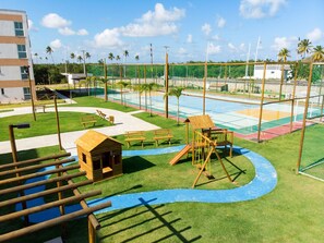 A playground with various play structures, a small wooden cabin, and a basketball court. - Flats no Muro Alto Clube (Ipojuca)