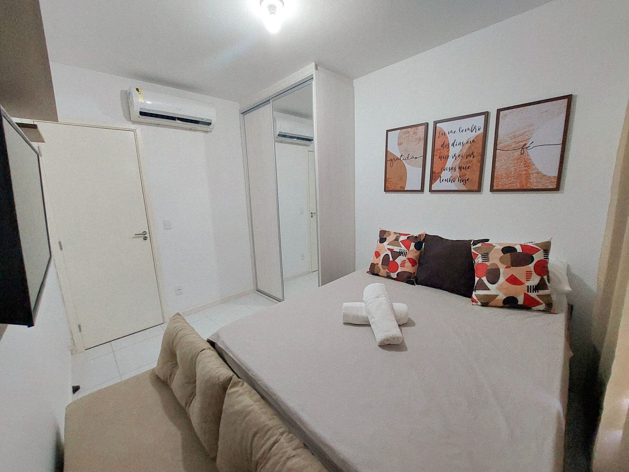 Un dormitorio con cama, almohadas, mesita de noche y aire acondicionado instalado en la pared.