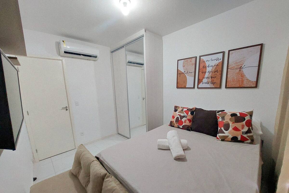 A bedroom with a bed, pillows, a bedside table, and a wall-mounted air conditioner.