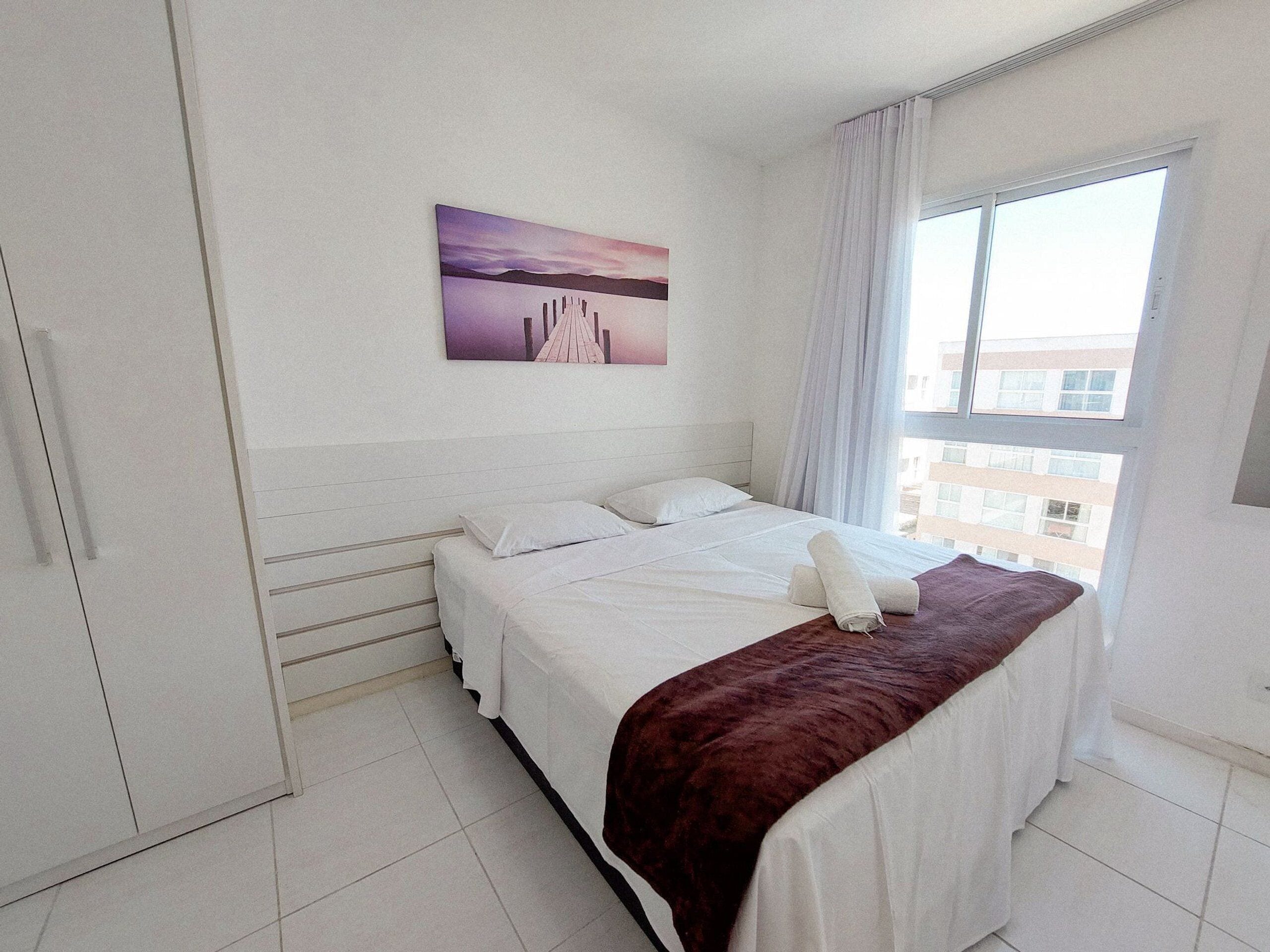 Habitación de hotel con una cama, una ventana con cortinas, un cuadro en la pared y vistas a edificios.