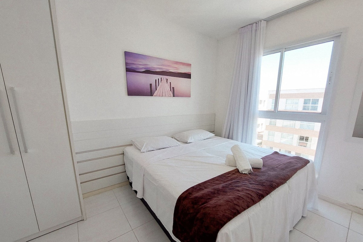 Habitación de hotel con una cama, una ventana con cortinas, un cuadro en la pared y vistas a edificios.