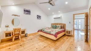 A bedroom with a wooden floor, a bed with a patterned bedspread, a desk with a chair, a ceiling fan, and wall-mounted air conditioning. - Cottage Like Suite w/ Private Hot Tub (Bass Lake)
