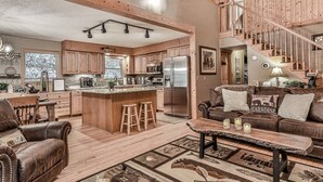 A spacious living area with a large island, leather furniture, and a staircase leading to an upper level. - Magical Forest Lodge-HotTub-Pool Table-Fireplace-Creek (Ellijay)