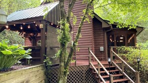 A rustic wooden cabin with a covered porch, wooden stairs, and a lattice fence. - Magical Forest Lodge-HotTub-Pool Table-Fireplace-Creek (Ellijay)