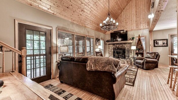 A cozy living room with a fireplace, wooden floors, a sofa, and a chandelier. - Magical Forest Lodge-HotTub-Pool Table-Fireplace-Creek (Ellijay)