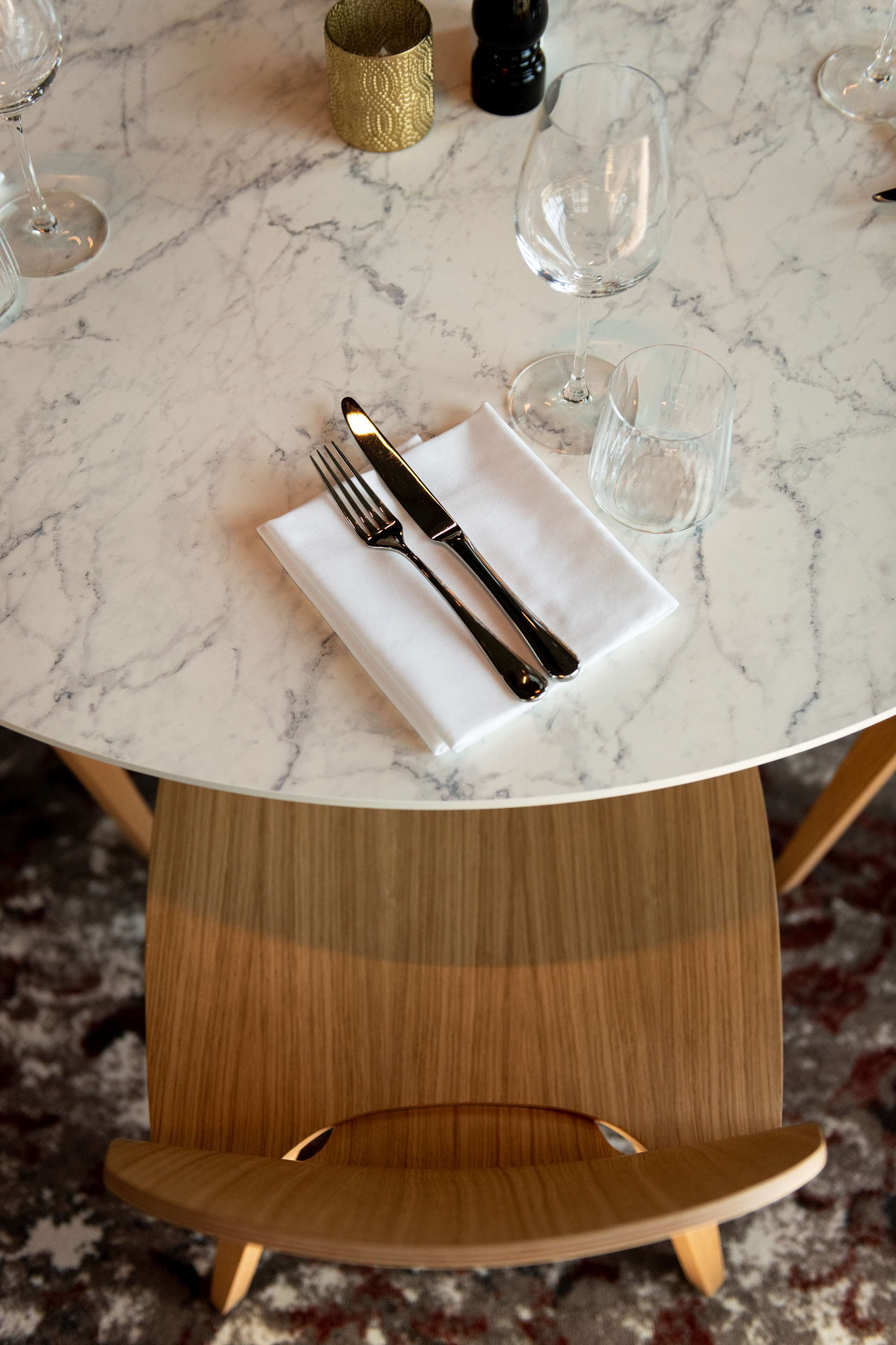 Una mesa de mármol con un mantel blanco, un tenedor y un cuchillo. Hay dos vasos y un salero sobre la mesa.