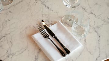 Una mesa de mármol con un mantel blanco, un tenedor y un cuchillo. Hay dos vasos y un salero sobre la mesa.