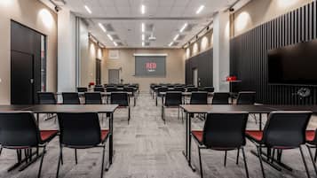 A conference room with rows of tables and chairs, a projector screen, and a large flat-screen TV.