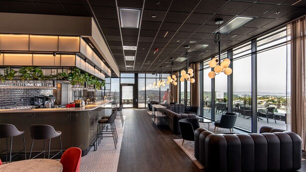 A modern interior with a bar area, seating, and large windows offering a view. - Radisson RED Oslo Økern (Oslo)