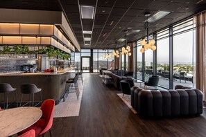 A modern interior with a bar area, seating, and large windows offering a view. - Radisson RED Oslo Økern (Oslo)