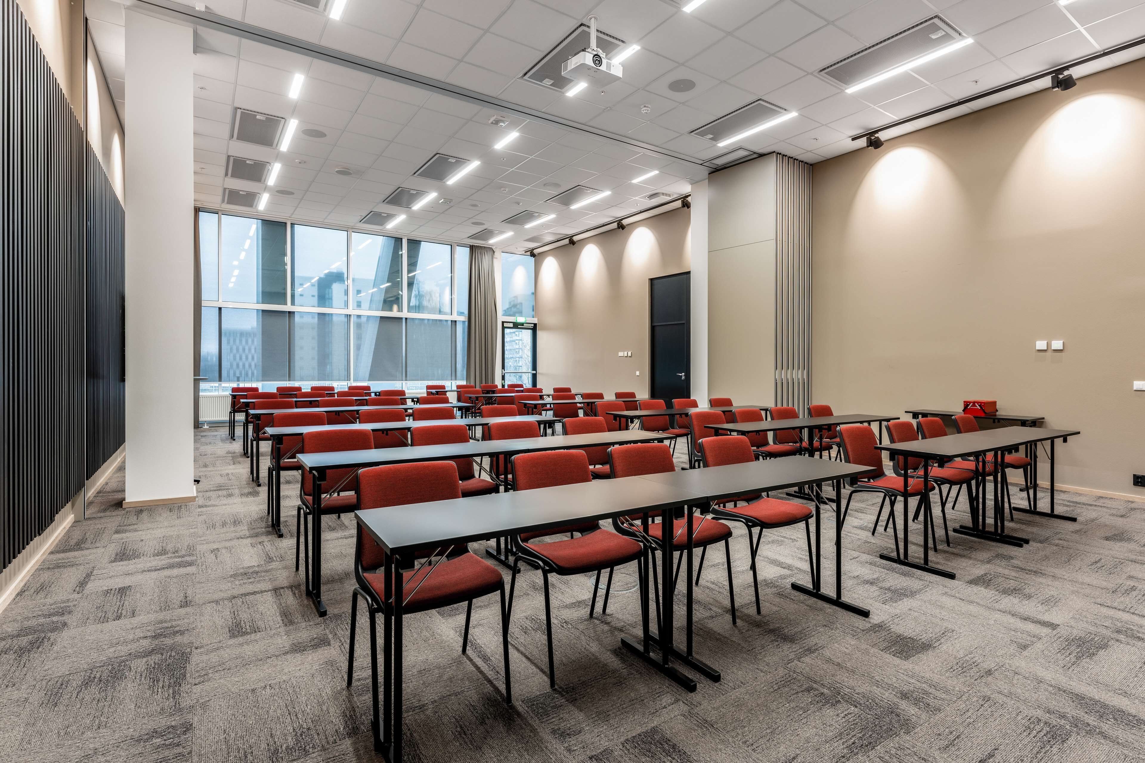 Un salón de conferencias con filas de mesas y sillas, ventanas amplias y un diseño moderno del techo.