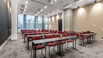Un salón de conferencias con filas de mesas y sillas, ventanas amplias y un diseño moderno del techo.