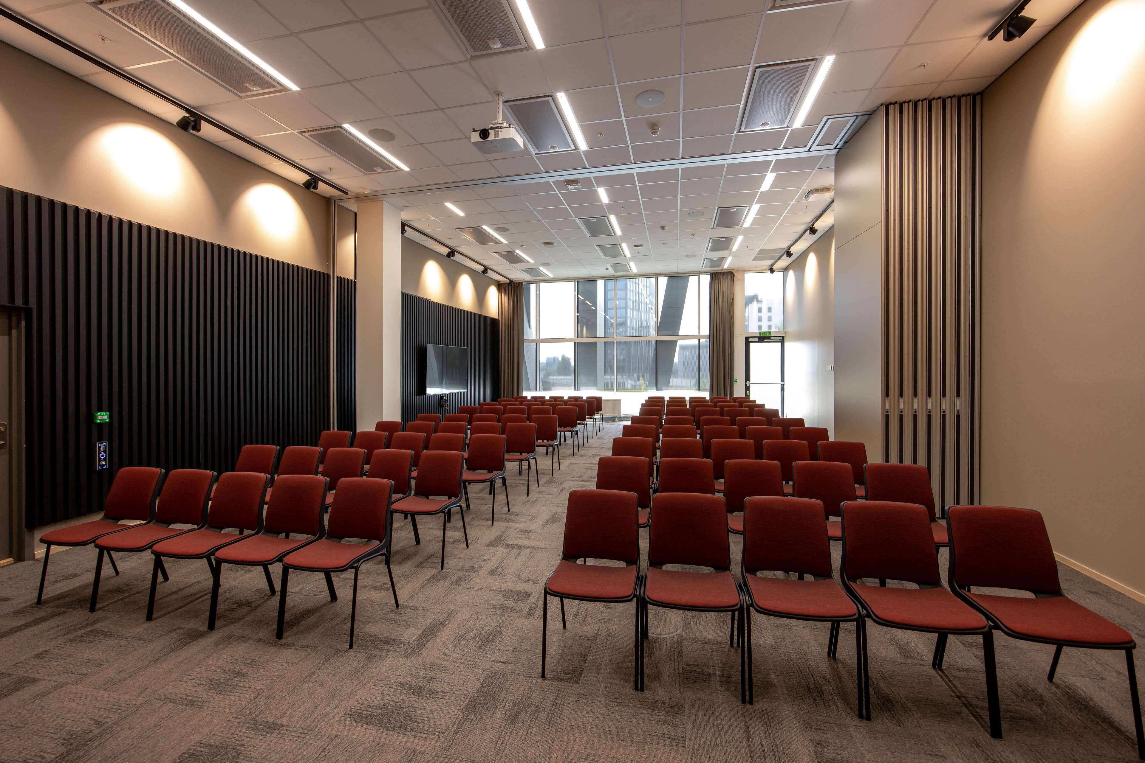 A conference room with rows of red chairs, a large window, and a modern ceiling design.