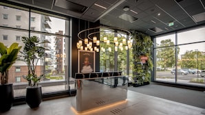 A reception desk with a modern design, large windows offering views of the city, and potted plants around the area. - Radisson RED Oslo Økern (Oslo)