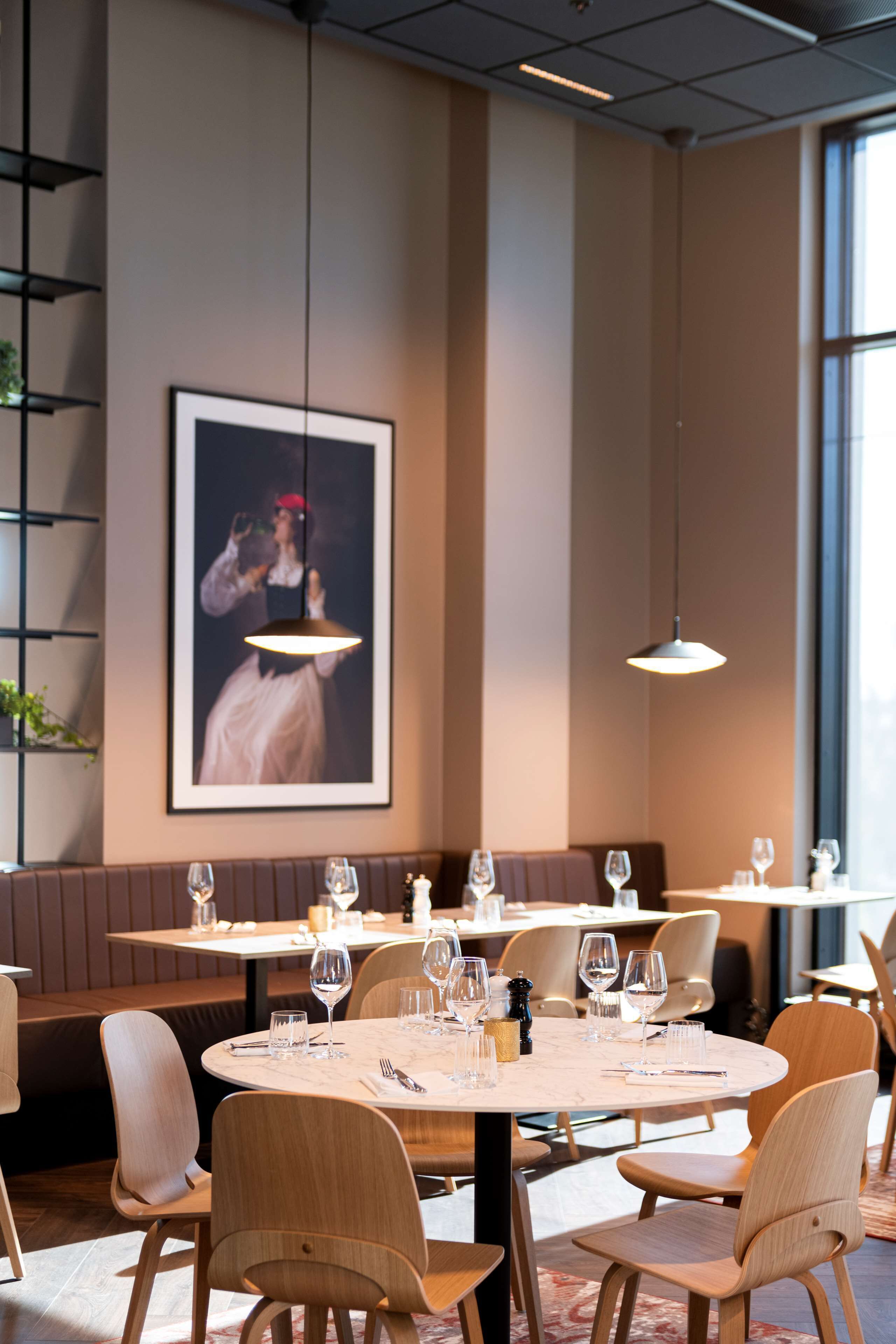 Un restaurante con mesas redondas, sillas de madera y un cuadro grande en la pared.