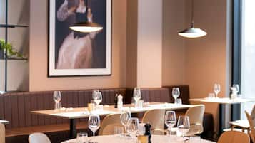 Un restaurante con mesas redondas, sillas de madera y un cuadro grande en la pared.