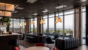 A modern lounge area with a bar, seating, and large windows offering a city view. - Radisson RED Oslo Økern (Oslo)