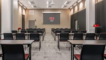 A conference room with rows of tables and chairs, a projector screen with the text "RED Radisson", and a door at the far end.