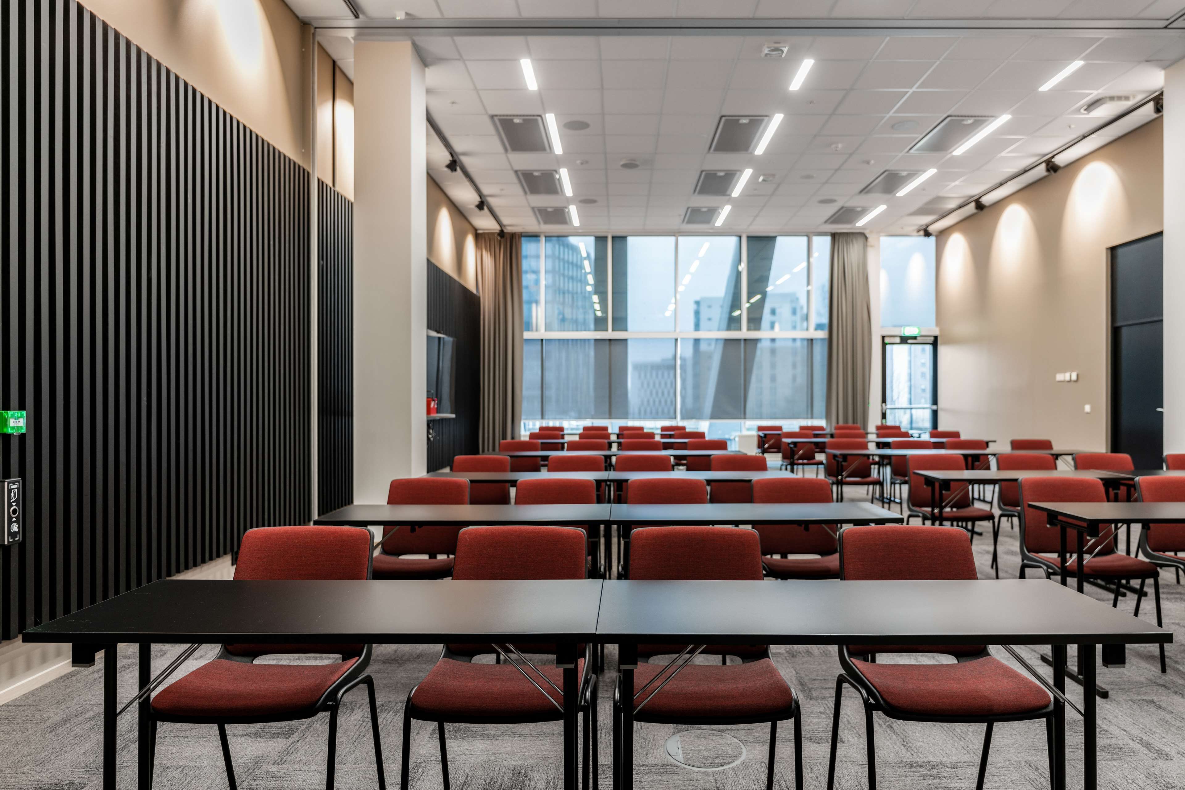 A conference room with rows of tables and chairs, large windows, and a modern ceiling design.