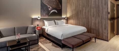 Un dormitorio moderno con cama, sofá, mesita de noche y una obra de arte en la pared.