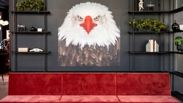A modern interior with a red sofa and three round tables, a large wall mural of an eagle, shelves with plants, and decorative items.