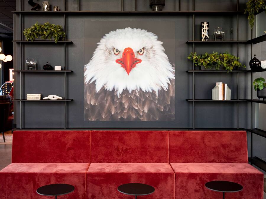 A modern interior with a red sofa and three round tables, a large wall mural of an eagle, shelves with plants, and decorative items.