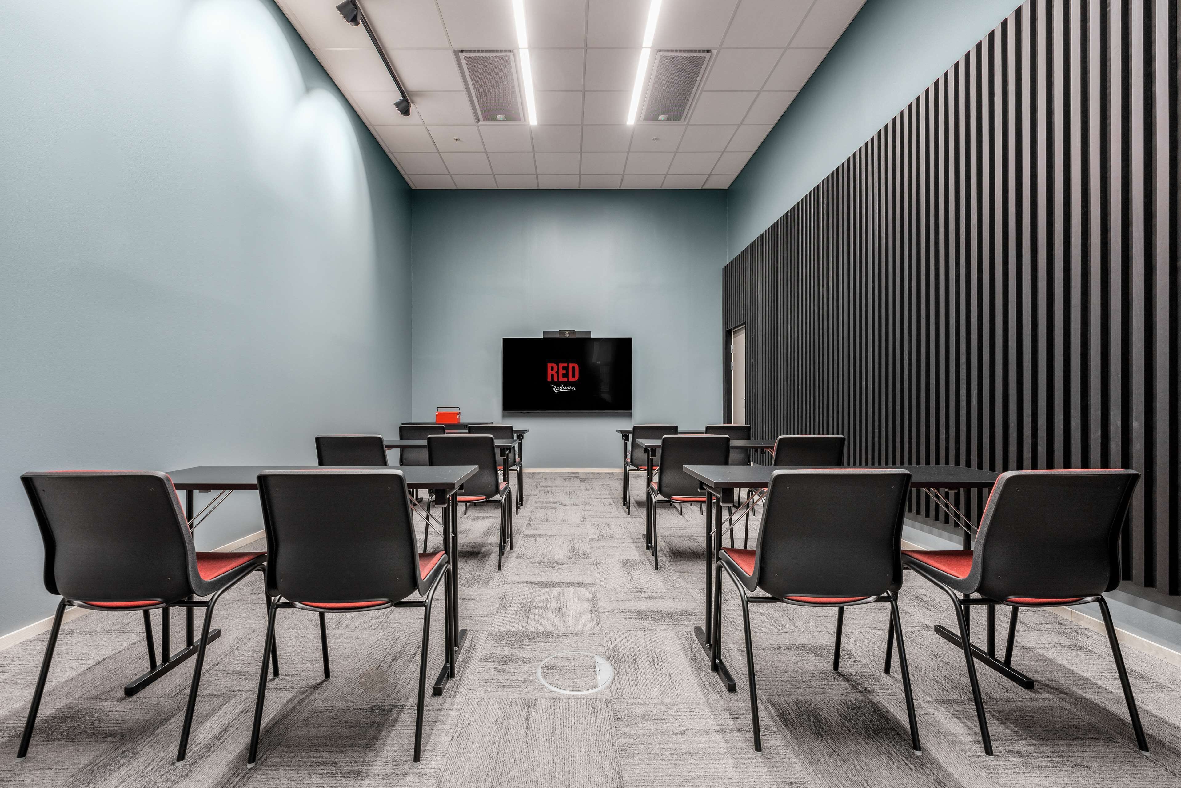 Un salón de conferencias con una pantalla grande mostrando la palabra “RED” y un diseño moderno y minimalista, con paredes grises y sillas negras.