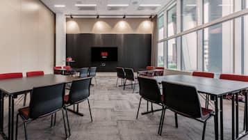 A conference room with a large screen, multiple tables, and chairs.