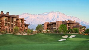 A golf course with a mountainous backdrop, featuring multi-story buildings with stone facades and balconies.