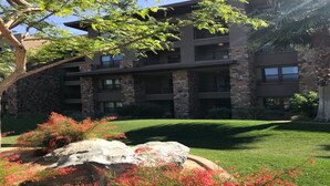 A multi-story building with stone facade and balconies, surrounded by well-maintained grass and flowering plants.