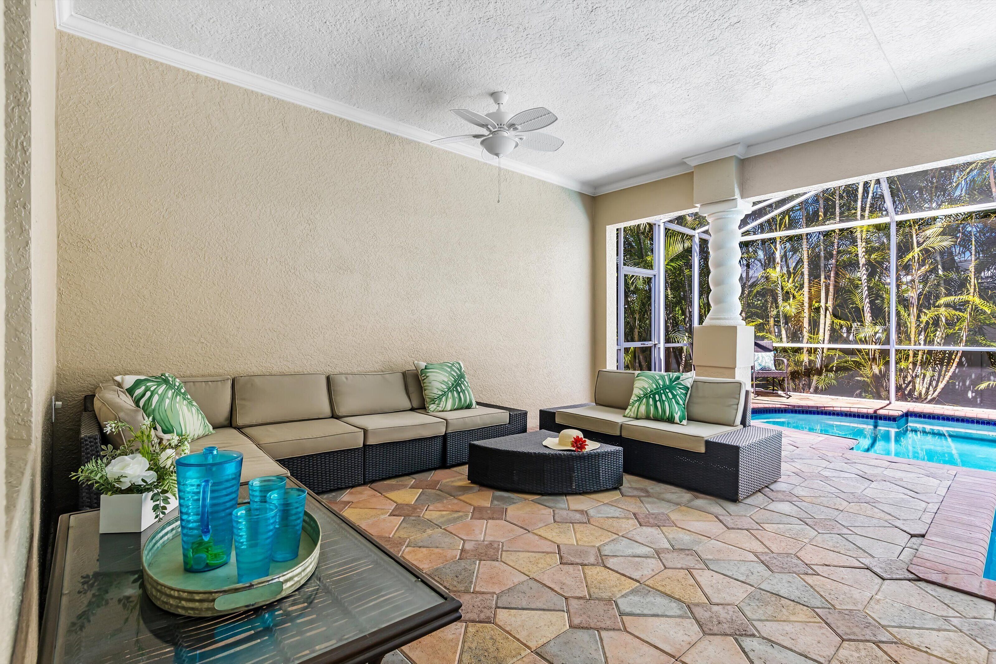 A sunlit patio with a pool, beige walls, and a ceiling fan.