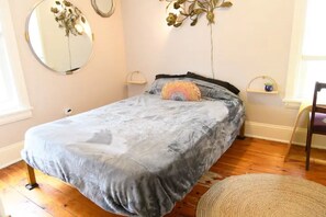 Ein Schlafzimmer mit einem Bett, einem runden Spiegel und einem kleinen Regal mit einer Pflanze.
