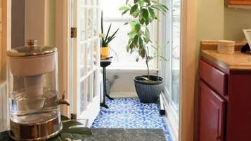 Un couloir étroit avec un plancher en bois, un petit tapis, une plante en pot et un coin cuisine avec des placards rouges et un évier.