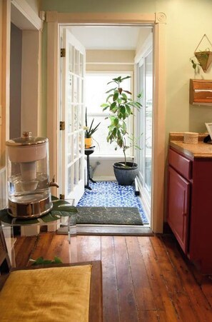 A narrow hallway with wooden flooring, a small rug, a potted plant, and a kitchen area with red cabinets and a sink.