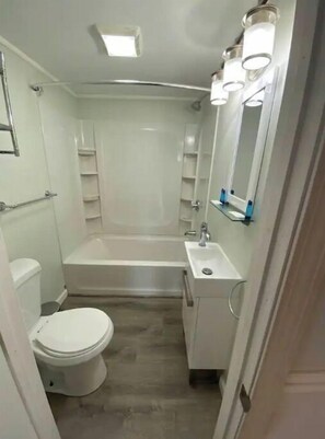 Een kleine, praktische badkamer met toilet, bad en wastafel.