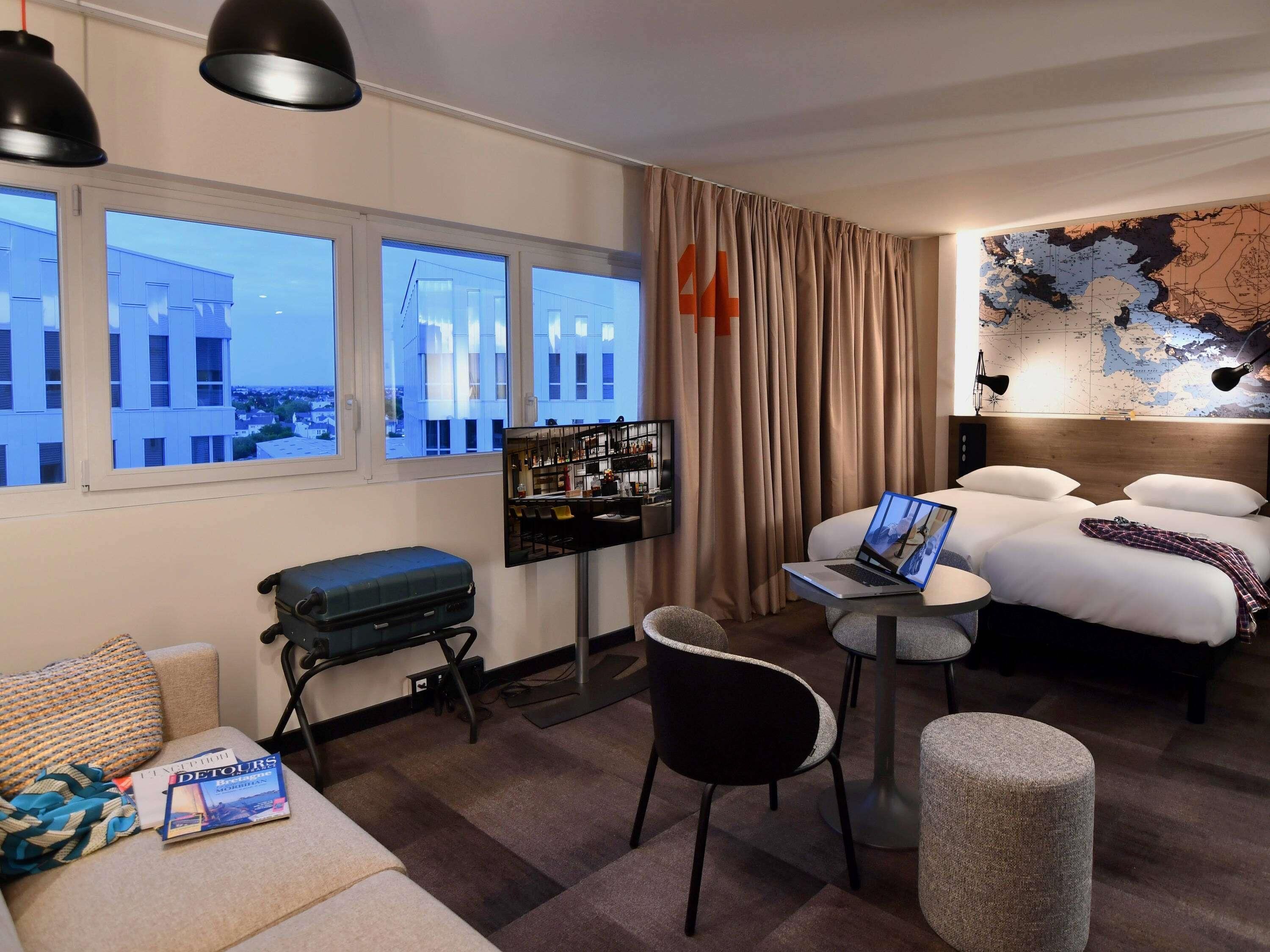 Una habitación de hotel con cama, escritorio, silla, maleta y un mapa en la pared.